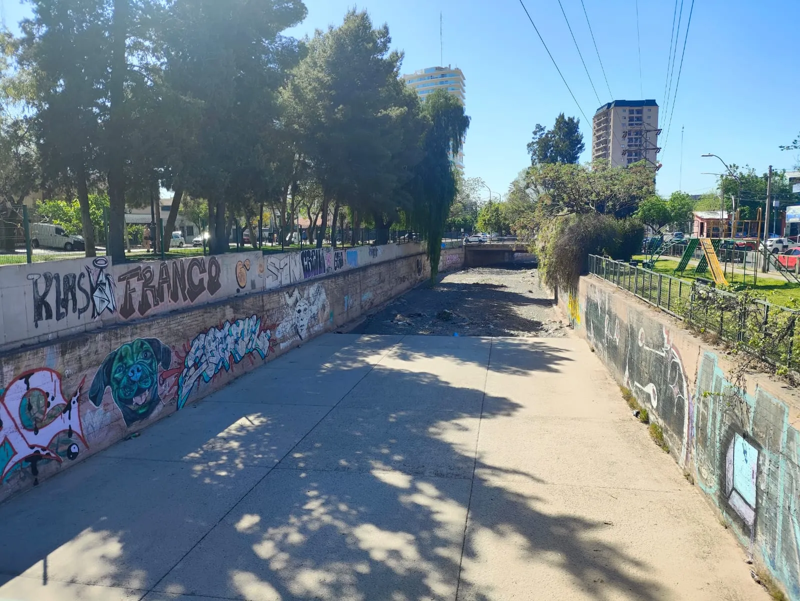 El Zanjón Frías hoy, visto hacia el este: losa de hormigón, ripio y muros con graffitis hasta el puente